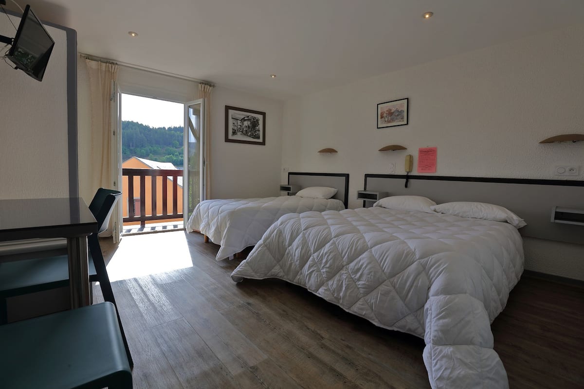 Une chambre d’hôtel avec deux lits, un bureau et un balcon donnant sur l’extérieur.