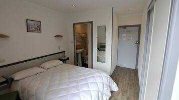 A hotel room with a large bed, a bedside table, a mirror, and a bathroom visible through an open door.