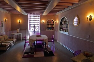 Um quarto aconchegante com uma mesa redonda, cadeiras roxas, um sofá e estantes de livros.
