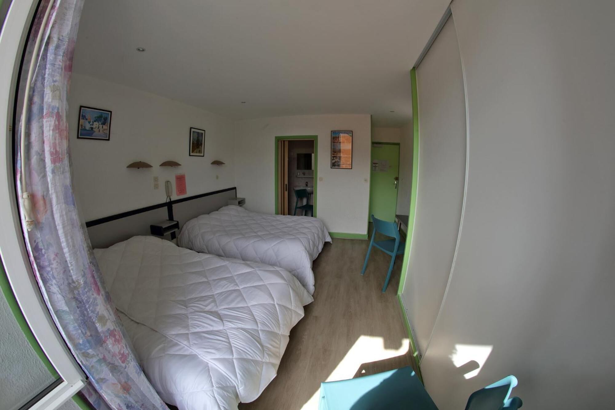 A room with two beds, a desk, and a chair. There is a door leading to another room.