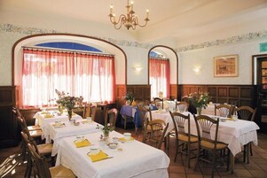 Restaurante com várias mesas preparadas para refeições, com cadeiras de madeira e toalhas de mesa brancas.