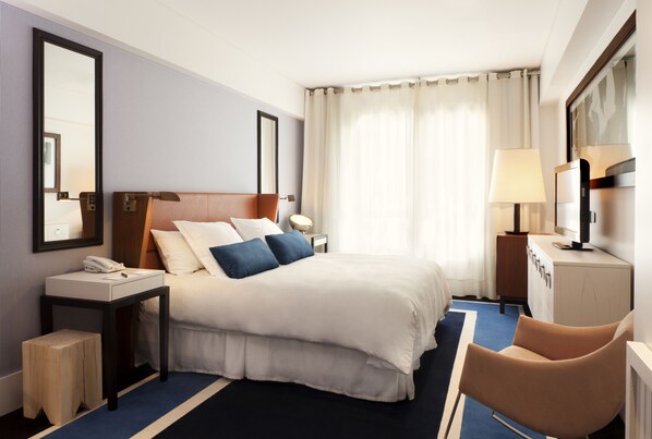 A hotel room with a large bed, bedside tables, a desk, a chair, a mirror, and a window with curtains. - Hotel Pulitzer (Buenos Aires)