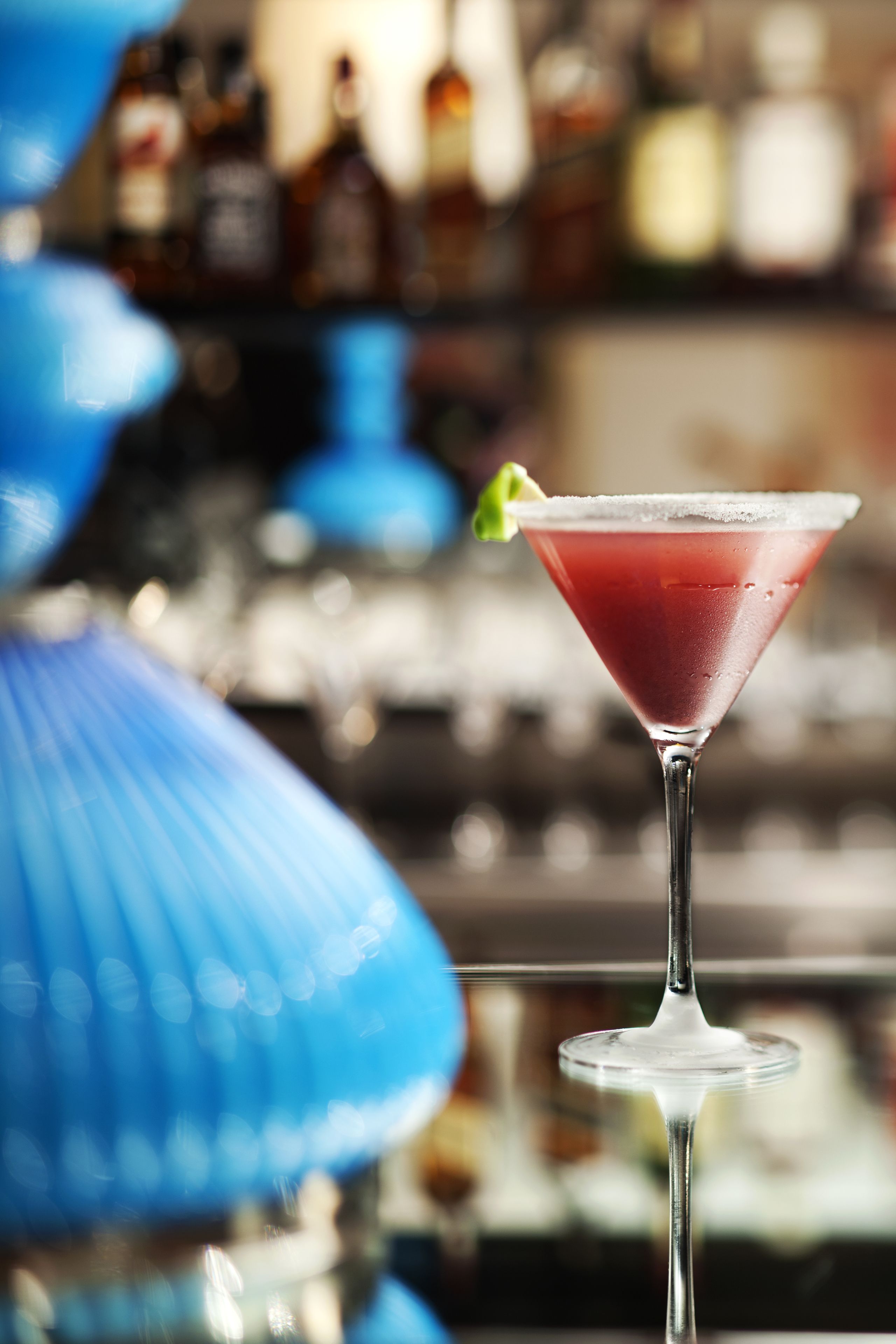 A martini glass with a red drink on a bar counter.