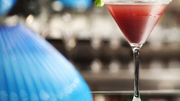 A martini glass with a red drink on a bar counter.