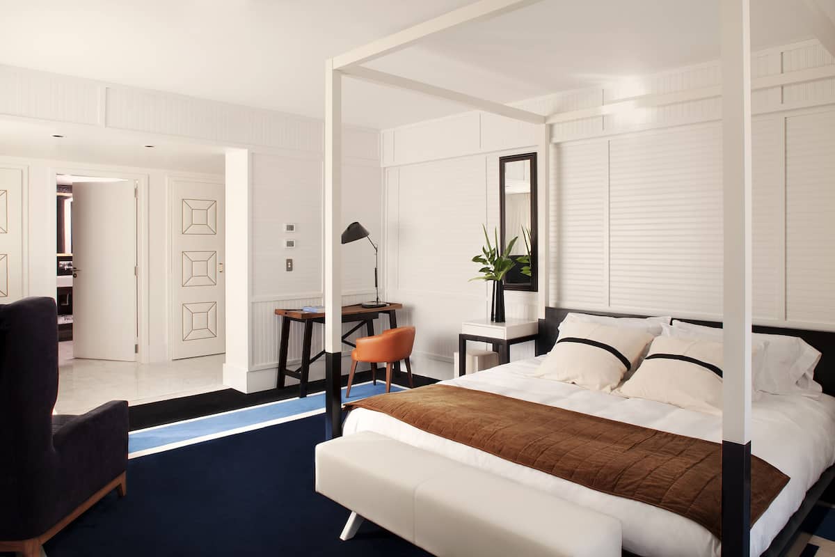 A modern bedroom with a four-poster bed, a desk, and a chair.