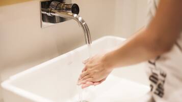 A person washing hands under a modern faucet in a bathroom.