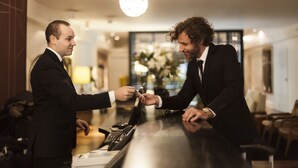 Two men in suits at a hotel reception, exchanging a card. - Hotel Pulitzer (Buenos Aires)