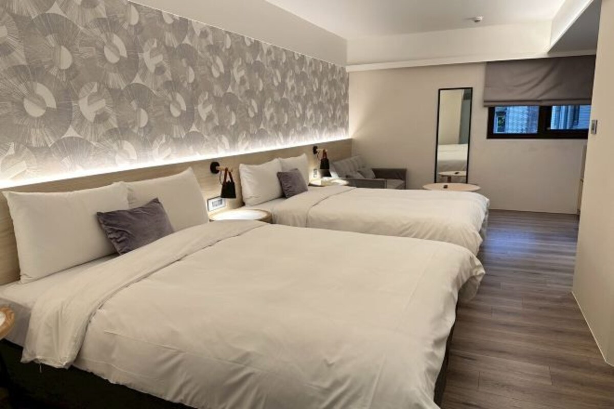 Habitación de hotel con dos camas, un espejo grande, una mesita de noche y una ventana.
