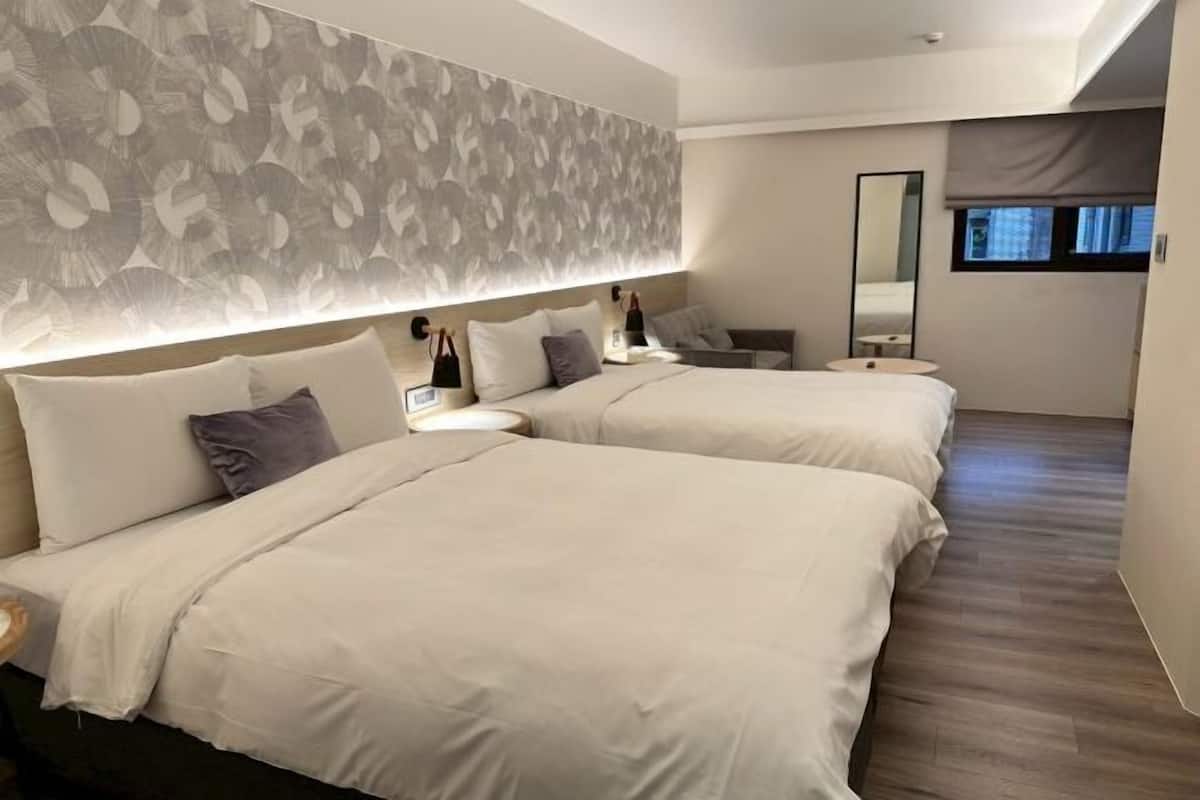 A hotel room with two beds, a large mirror, a bedside table, and a window.