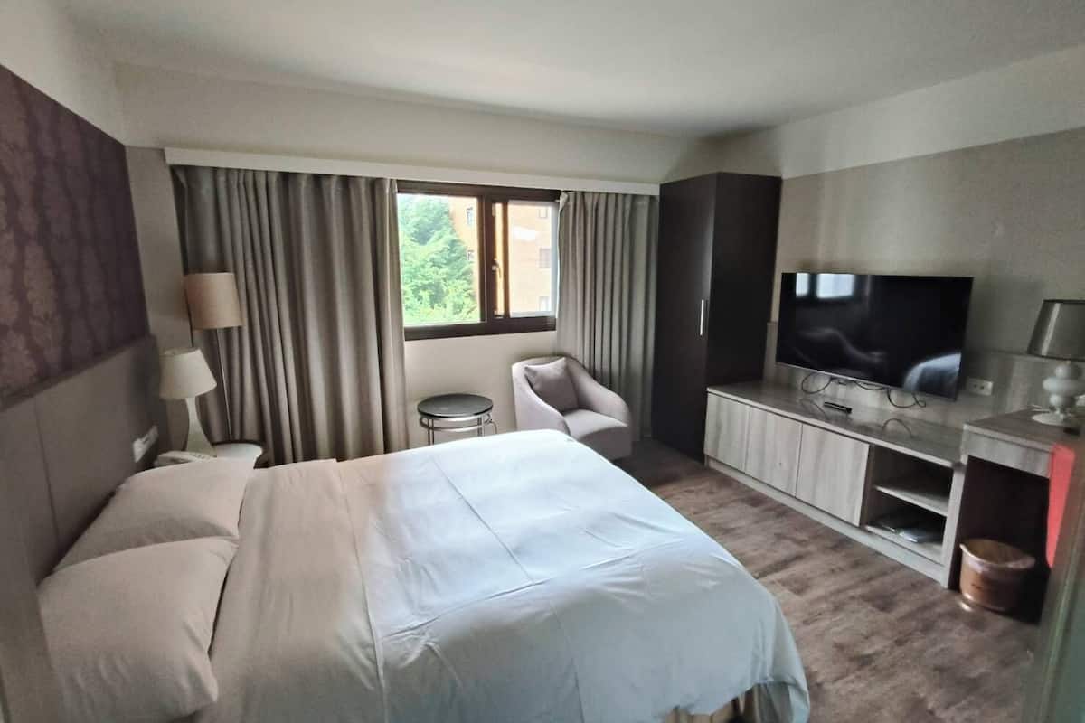 A hotel room with a bed, a TV, a desk, a chair, and a window.