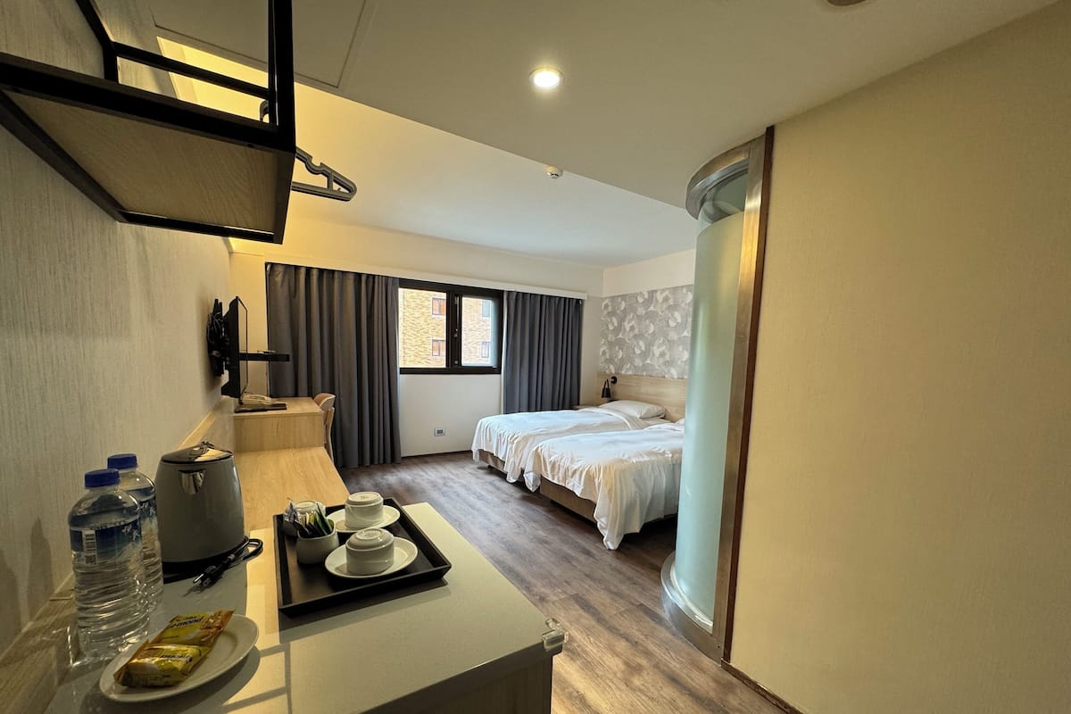 A hotel room with a bed, a desk with a tray of breakfast items, a water dispenser, and a window with curtains.