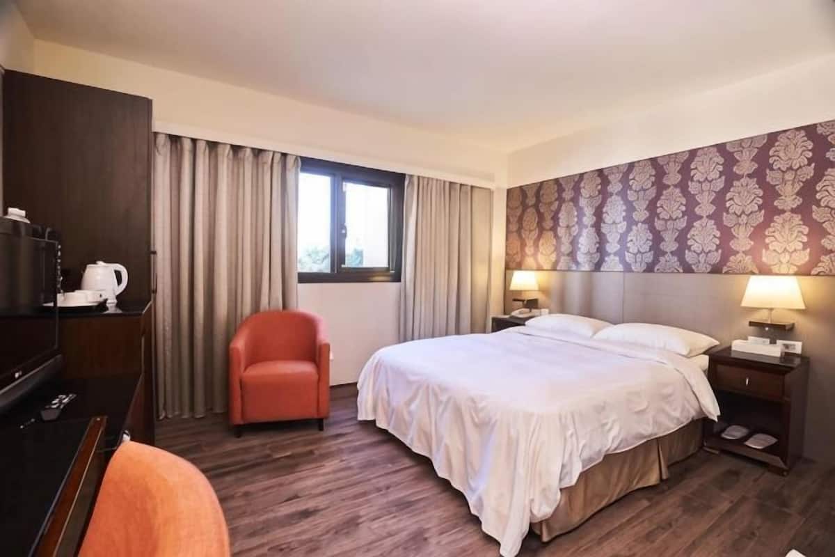 A hotel room with a bed, a chair, a desk with a lamp, and a TV.