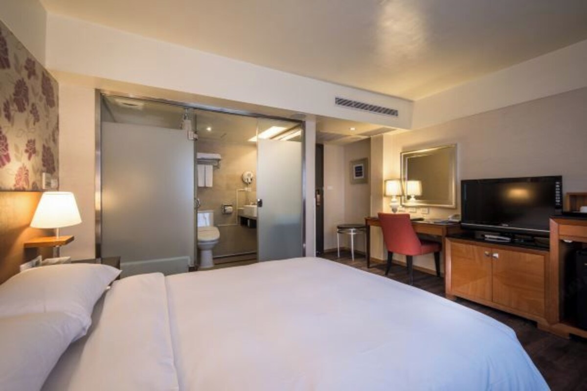 Habitación de hotel con una cama grande, un escritorio con silla, televisión y baño visible a través de una puerta abierta.