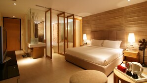 Ein modernes Hotelzimmer mit einem großen Bett, Nachttischen, einem Fernseher und einem Badezimmer mit Glasabtrennung.