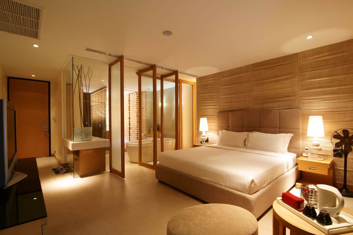 Une chambre d’hôtel moderne dotée d’un grand lit, de tables de chevet, d’une télévision et d’une salle de bain séparée par une paroi en verre.