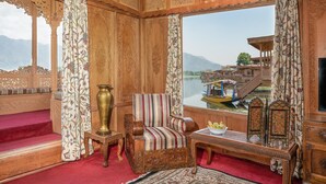 Una habitación con paneles de madera ornamentados, un ventanal con vista a un barco en un río, una alfombra roja y una silla tradicional.