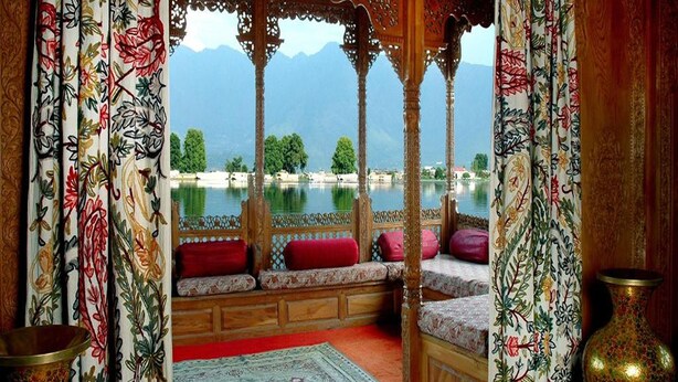 Una habitación tradicional con muebles de madera ornamentados, vista a un lago y cortinas decorativas.