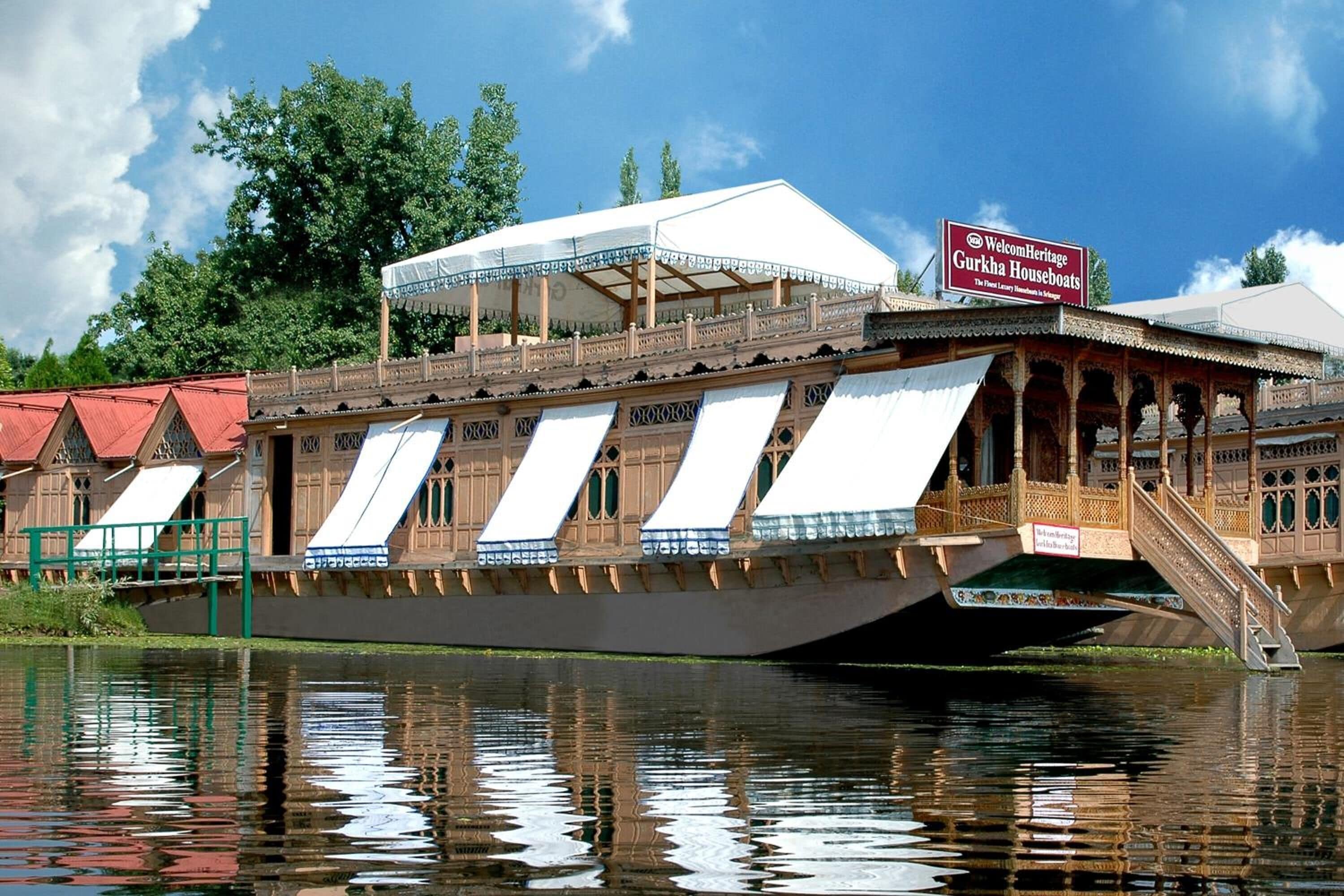 A traditional wooden houseboat with a covered upper deck, a signboard, and a bridge leading to it.