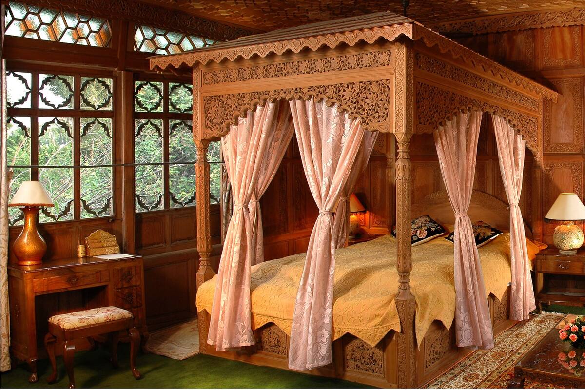 A four-poster canopy bed with floral curtains, a wooden desk with a lamp, and a floral-patterned armchair.