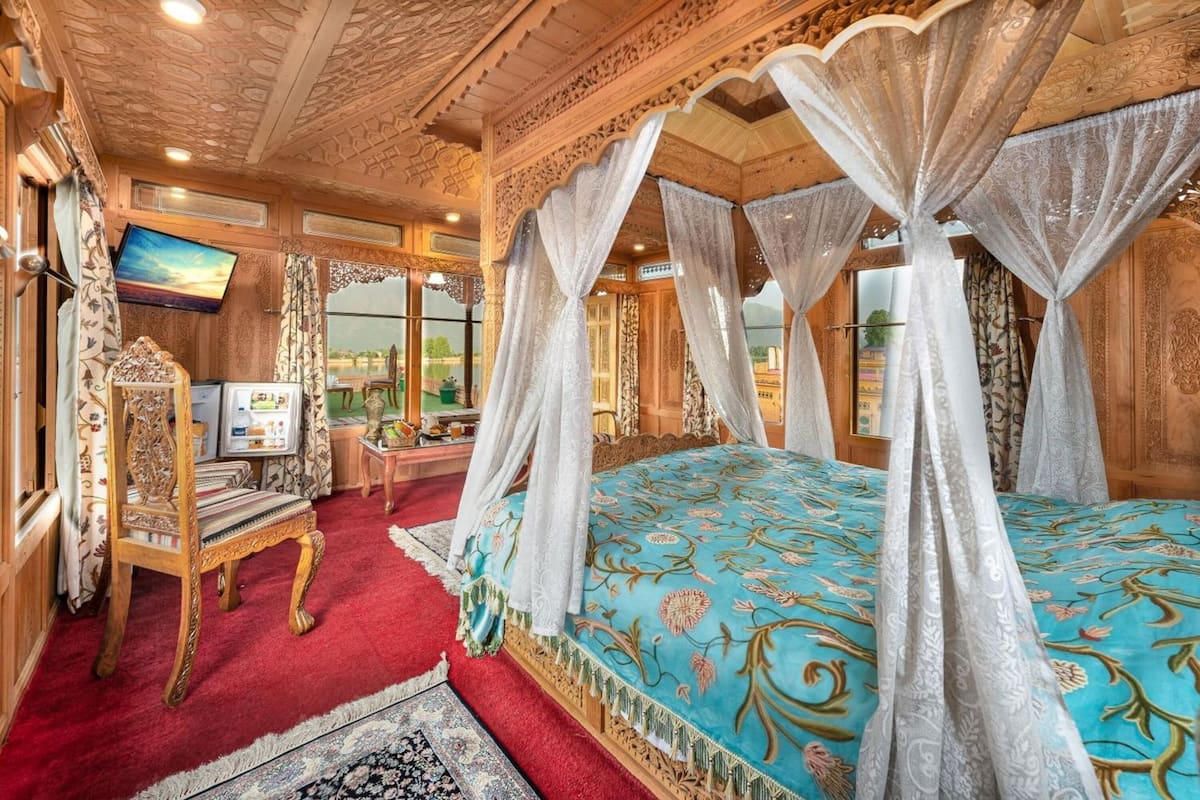 A room with a four-poster bed, a desk with a computer, and a large window.