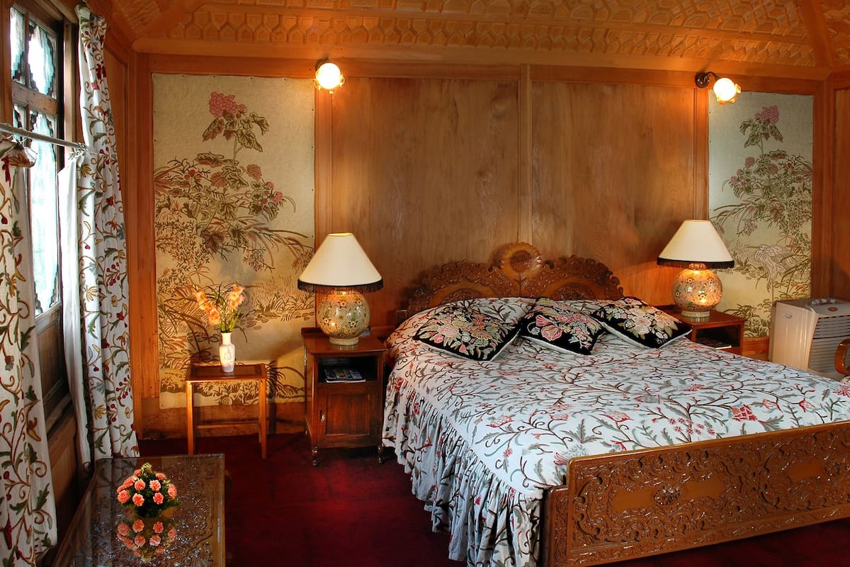 A traditional room with a wooden bed, two bedside tables with lamps, a chair, and a view of a lake through the window.