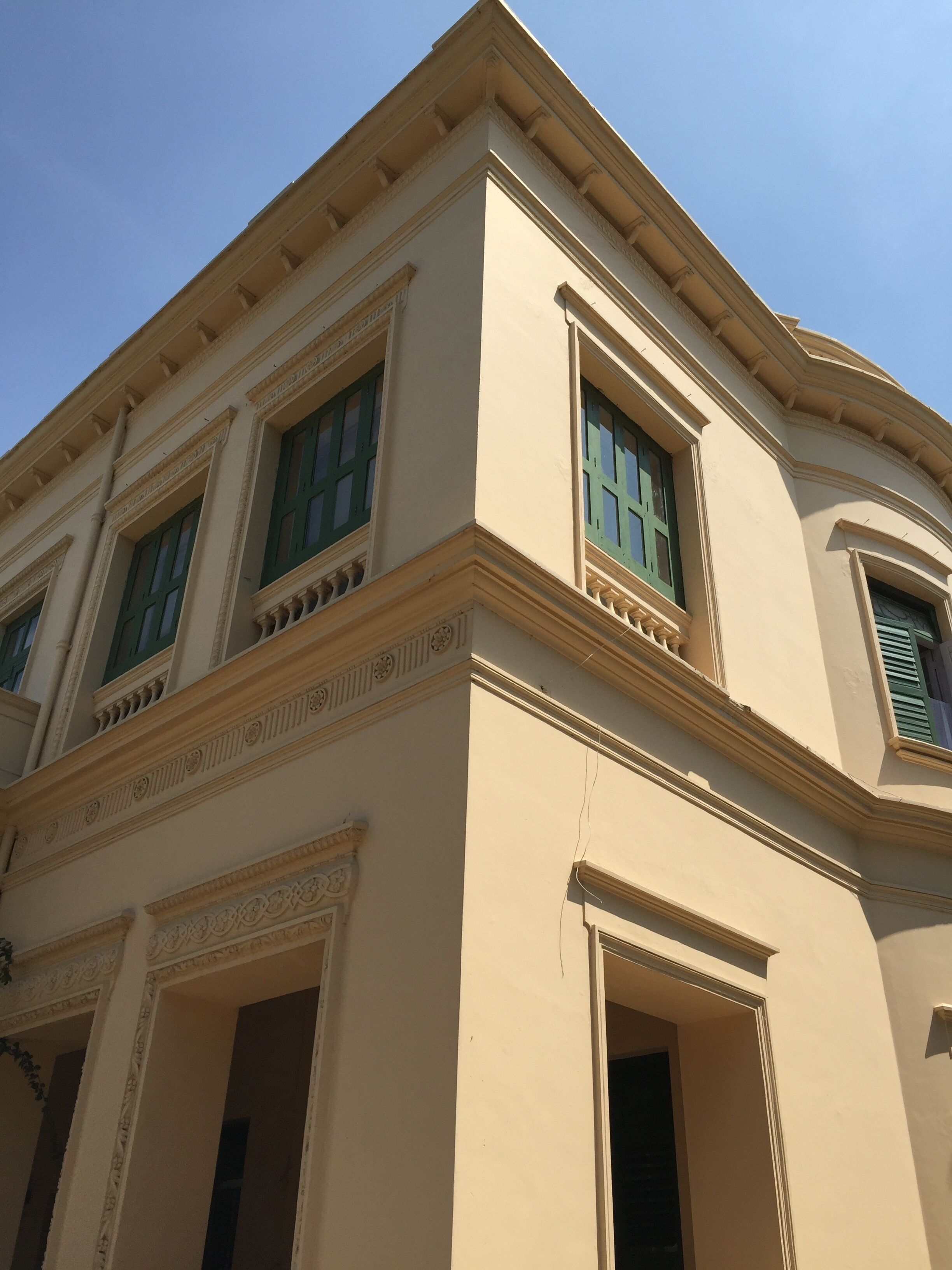 A building with classical architecture, featuring a symmetrical facade, large windows with green shutters, and decorative moldings.