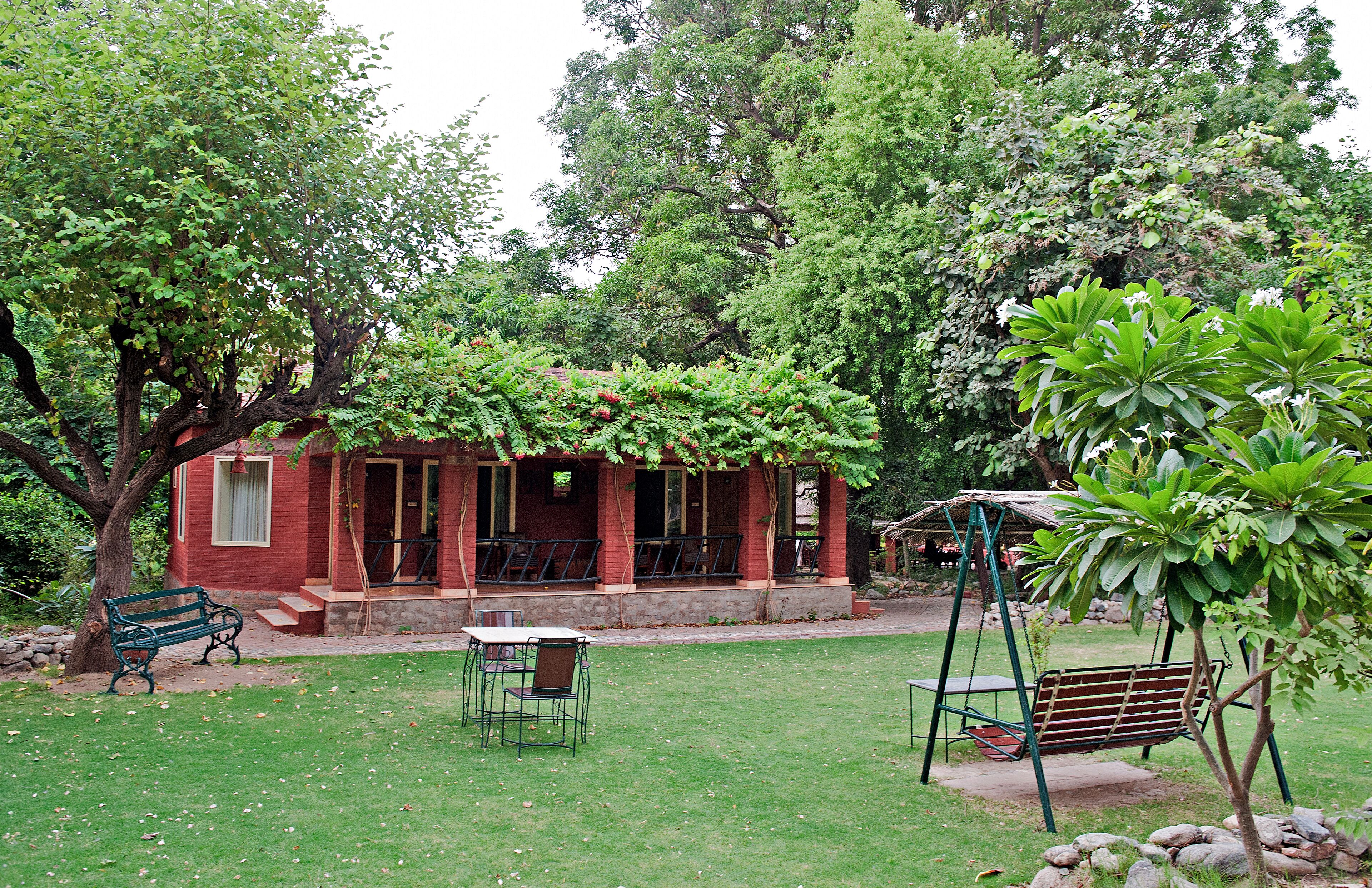 A red building with a porch, surrounded by trees and a grassy lawn.