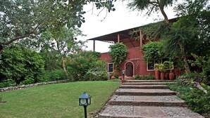 Un sendero de ladrillo que conduce a un edificio con entrada cubierta, rodeado de abundante vegetación y un césped cuidado.