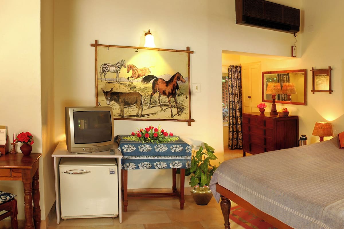 Habitación de hotel con cama, escritorio, refrigerador, televisión y obras de arte en las paredes.