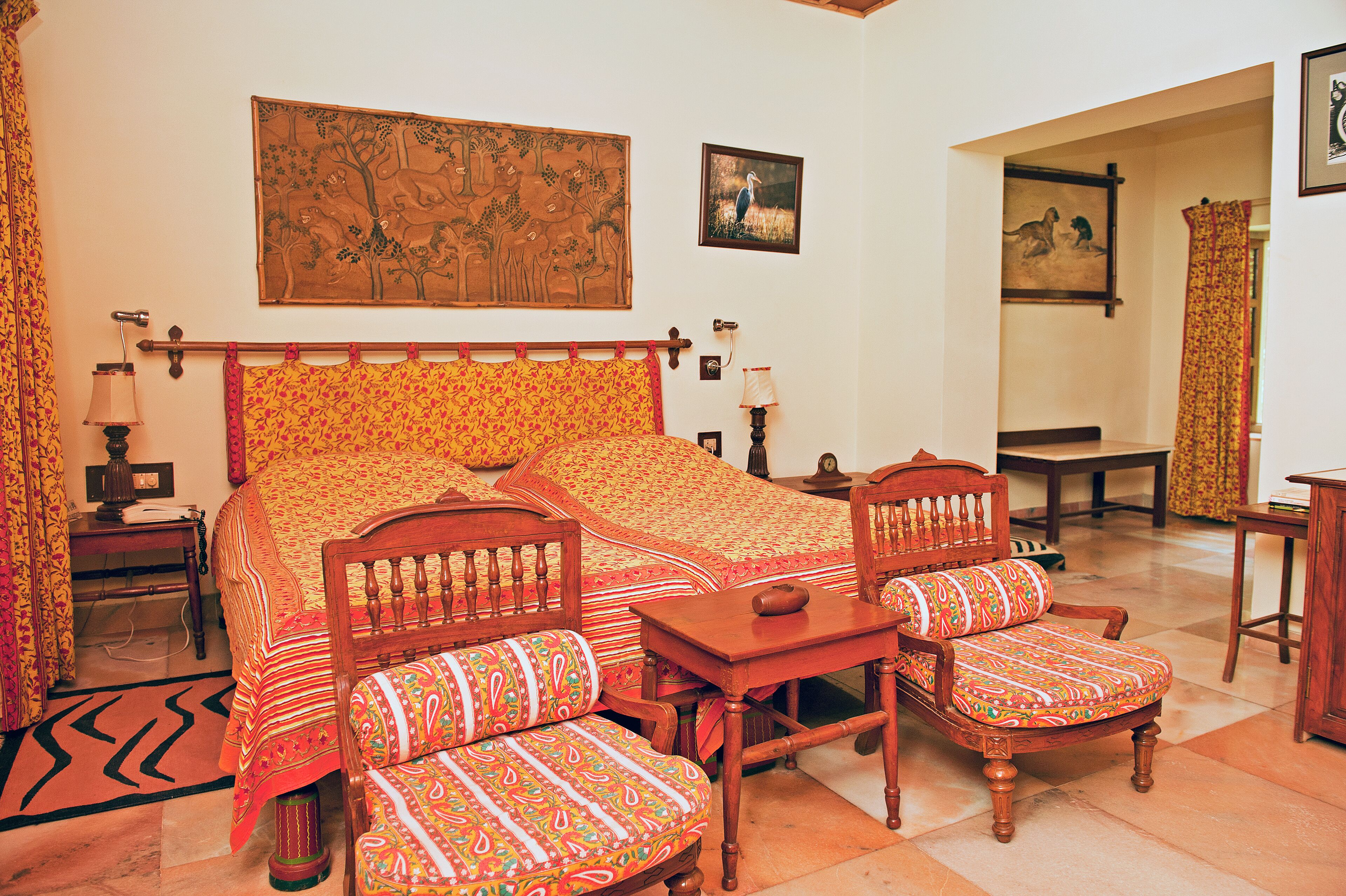Une chambre traditionnelle avec un lit, deux chaises en bois, une petite table et un tableau au mur.