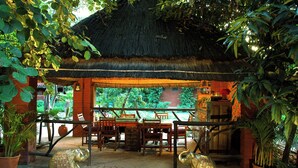 Un espacio de comedor al aire libre con techo de paja, muebles de madera y estatuas de elefantes.