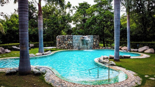 Una piscina con una cascada de piedra, rodeada de palmeras y un césped bien cuidado.