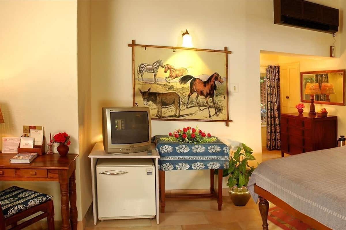 Habitación de hotel con cama, escritorio, televisor, refrigerador y obras de arte en las paredes.