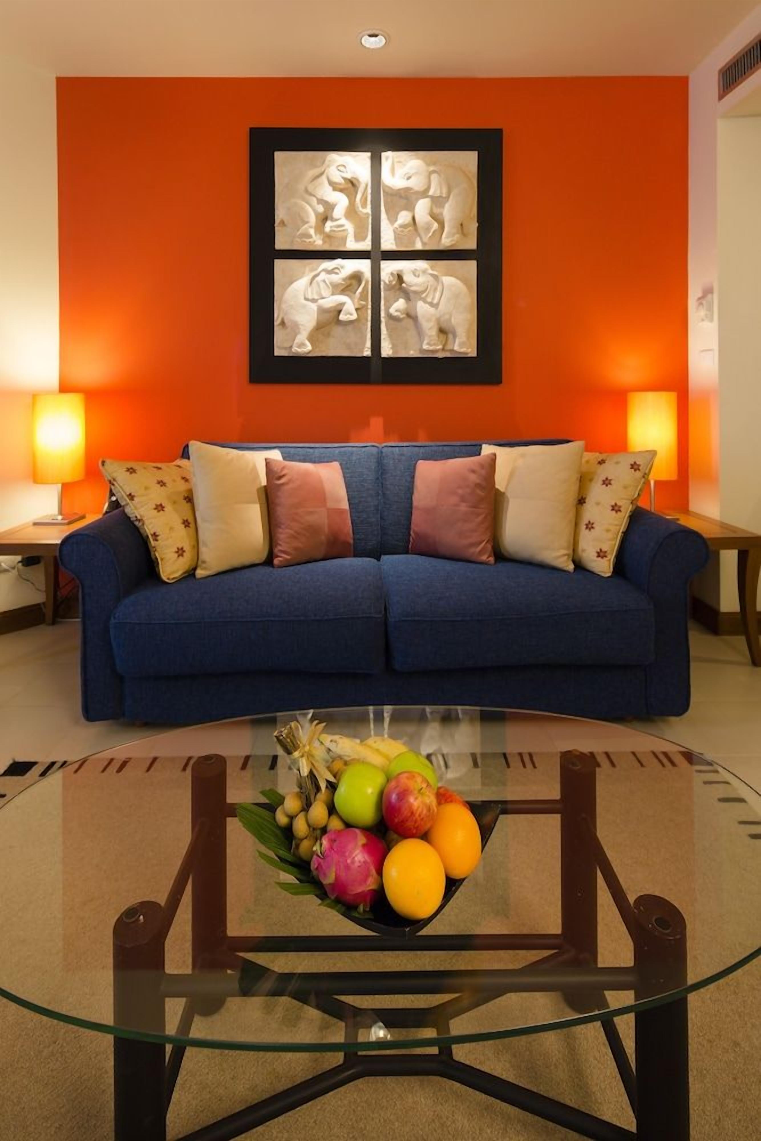 A room with a blue sofa, two wall-mounted lamps, and a glass coffee table with fruit.