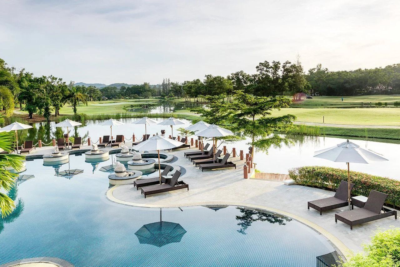 A resort pool area with lounge chairs and umbrellas, surrounded by a golf course and trees.