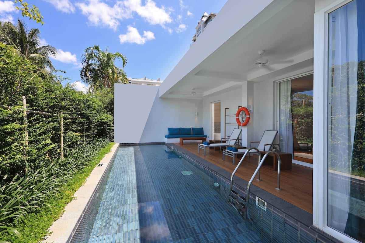 A modern outdoor pool area with a glass barrier, a blue sofa, and a lifebuoy.
