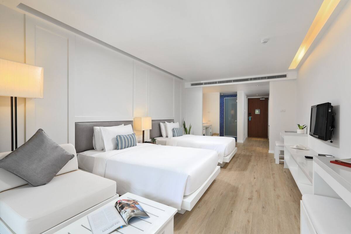 A hotel room with three beds, a sofa, a TV, and a desk with a lamp.