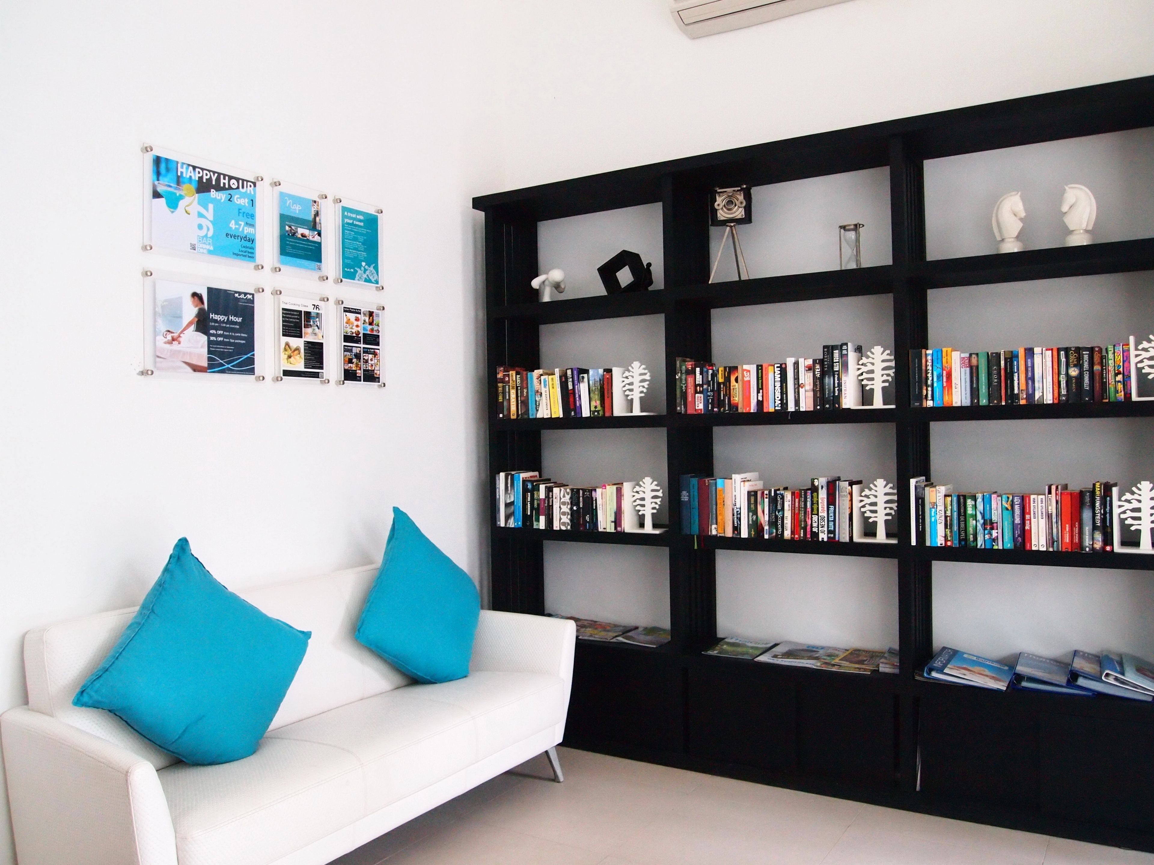 Ein modernes Wohnzimmer mit einem weißen Sofa, zwei blauen Kissen und einem schwarzen Bücherregal, das mit Büchern und Dekoration gefüllt ist.