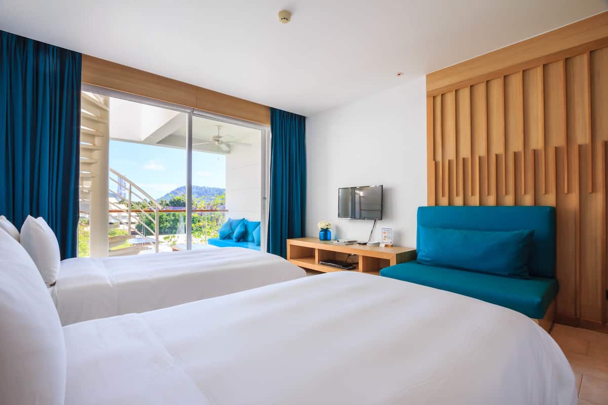 A hotel room with two beds, a TV, a sofa, and a view of a staircase and greenery outside.
