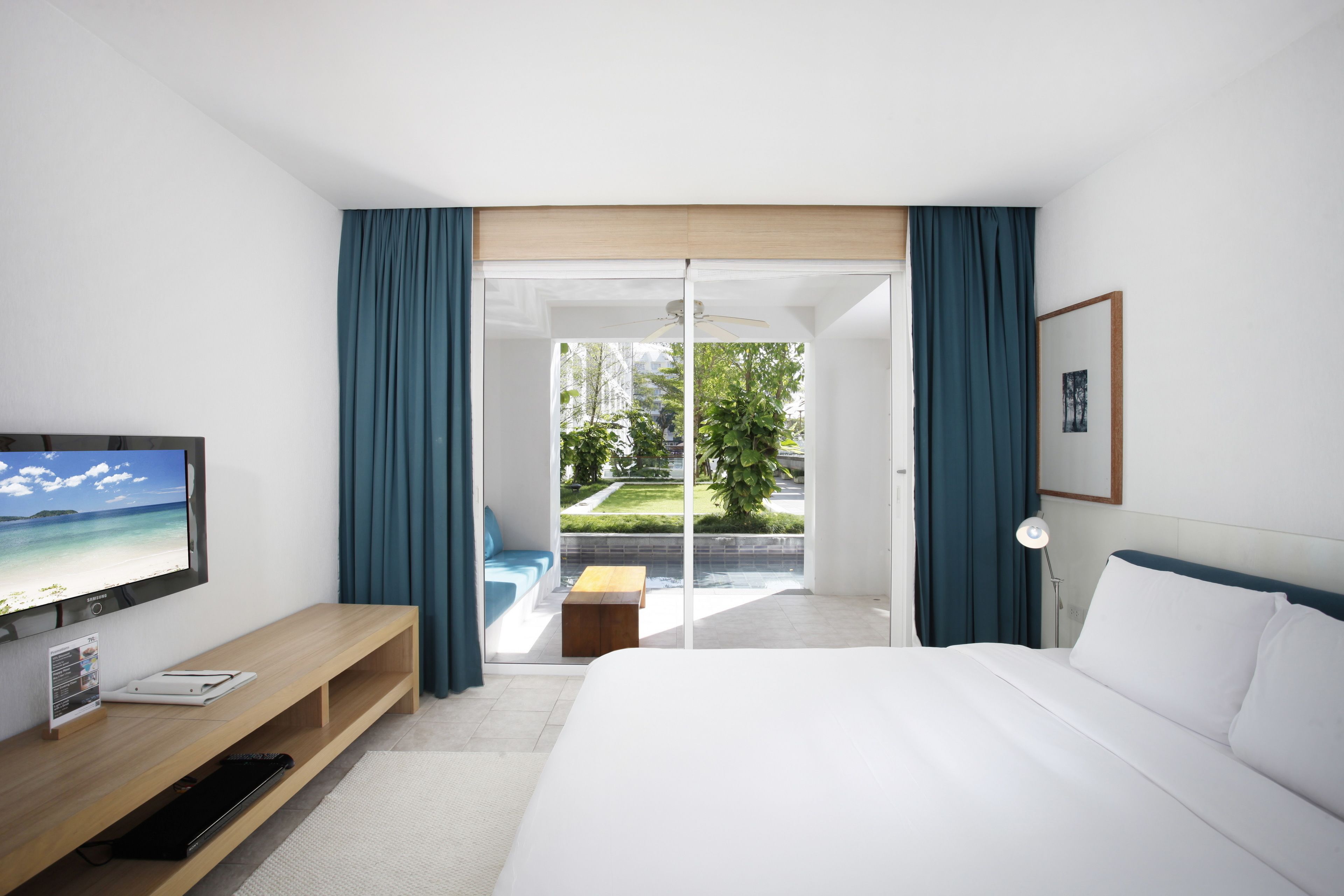 Habitación de hotel con cama, televisor, escritorio y vista a un jardín a través de una puerta corrediza.