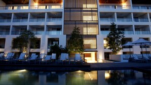 Un hotel moderno con zona de piscina, varios balcones y tumbonas.