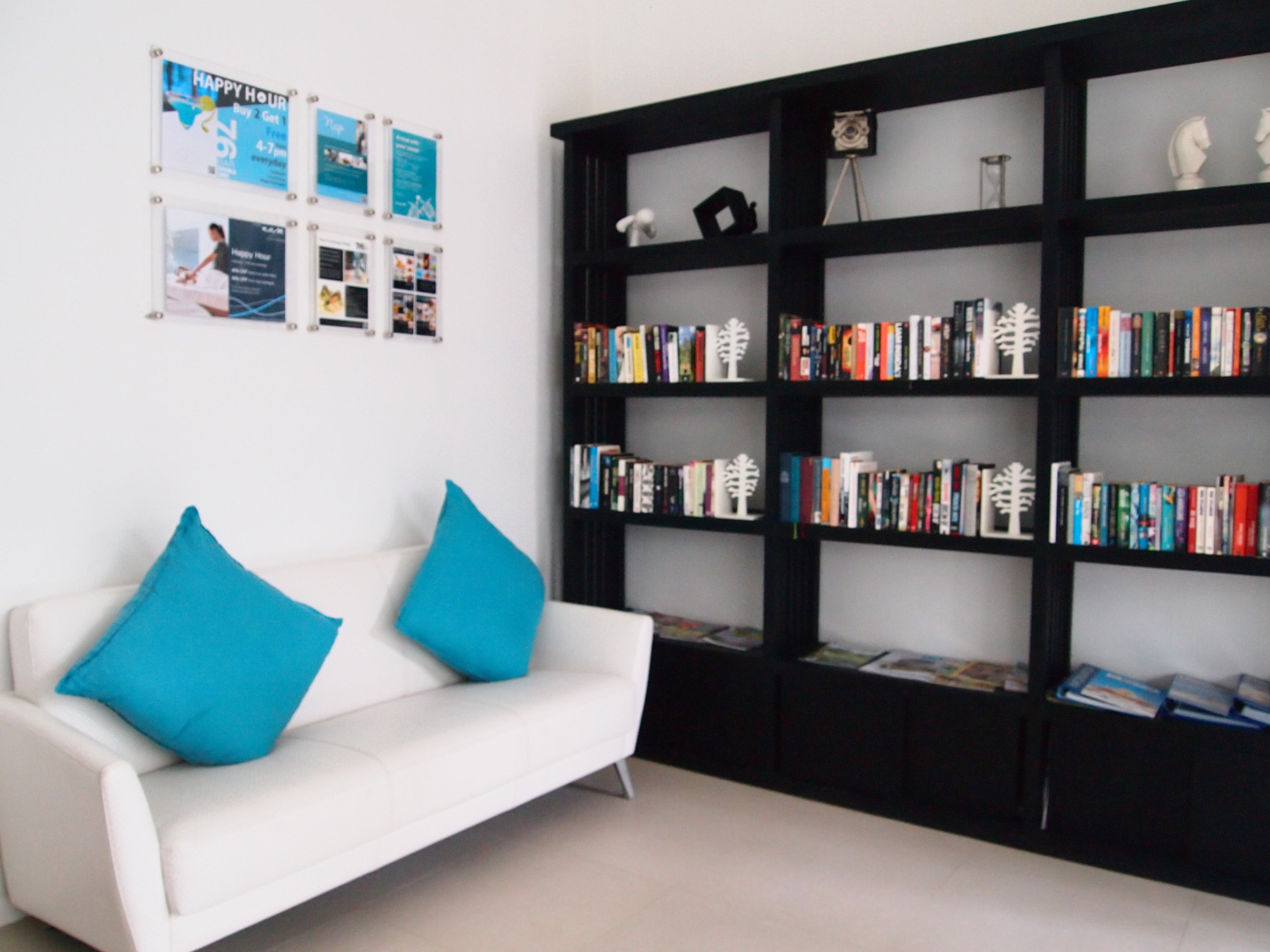 A modern living room with a white sofa and teal cushions, a black bookshelf filled with books, and a wall with multiple framed pictures.