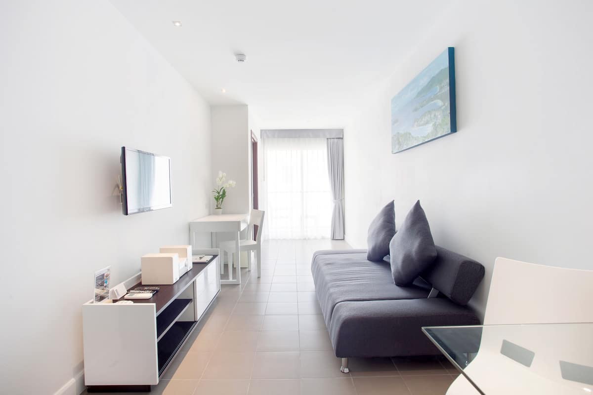 A modern, minimalist living room with a grey sofa, a small white table, and a TV mounted on the wall.