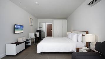 A modern hotel room with a large bed, a desk, a chair, a TV, and a bedside table with a lamp.