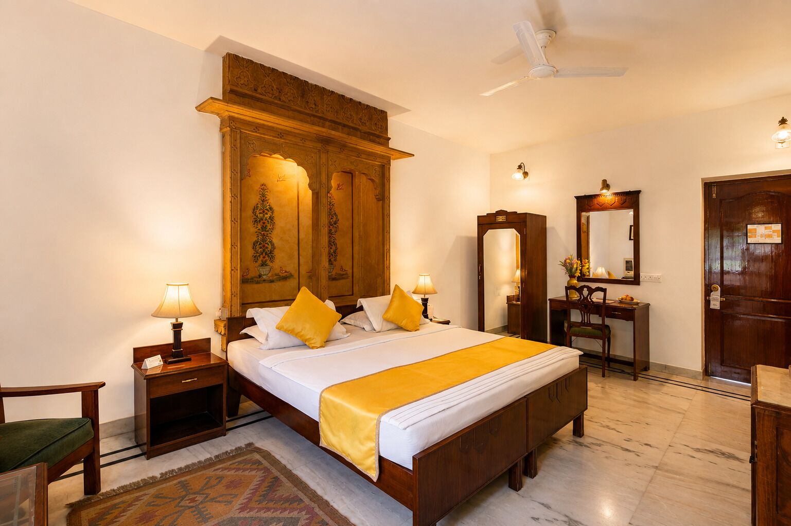 Une chambre d’hôtel avec un grand lit, des lampes de chevet, une armoire en bois, un bureau avec une chaise, un miroir et une porte.