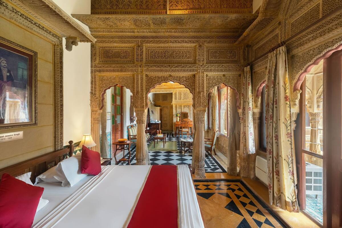 A room with a bed, a dining table, and chairs, with intricate ceiling and wall designs.
