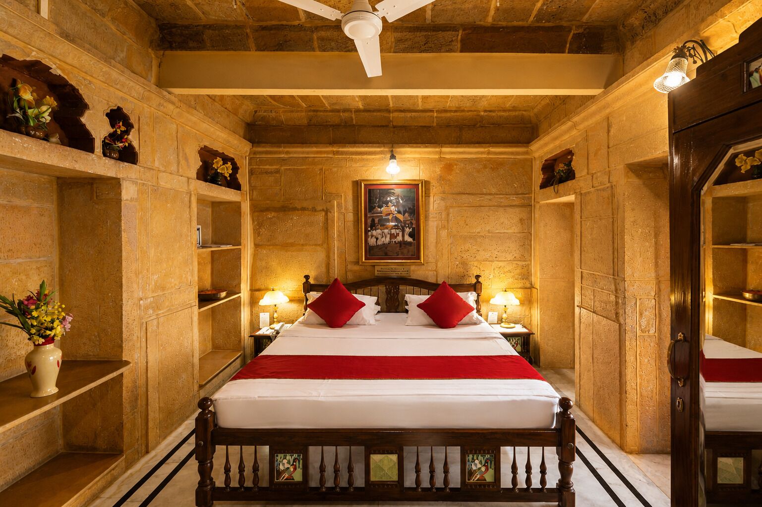 A room with a bed, two bedside lamps, a ceiling fan, and a painting on the wall.