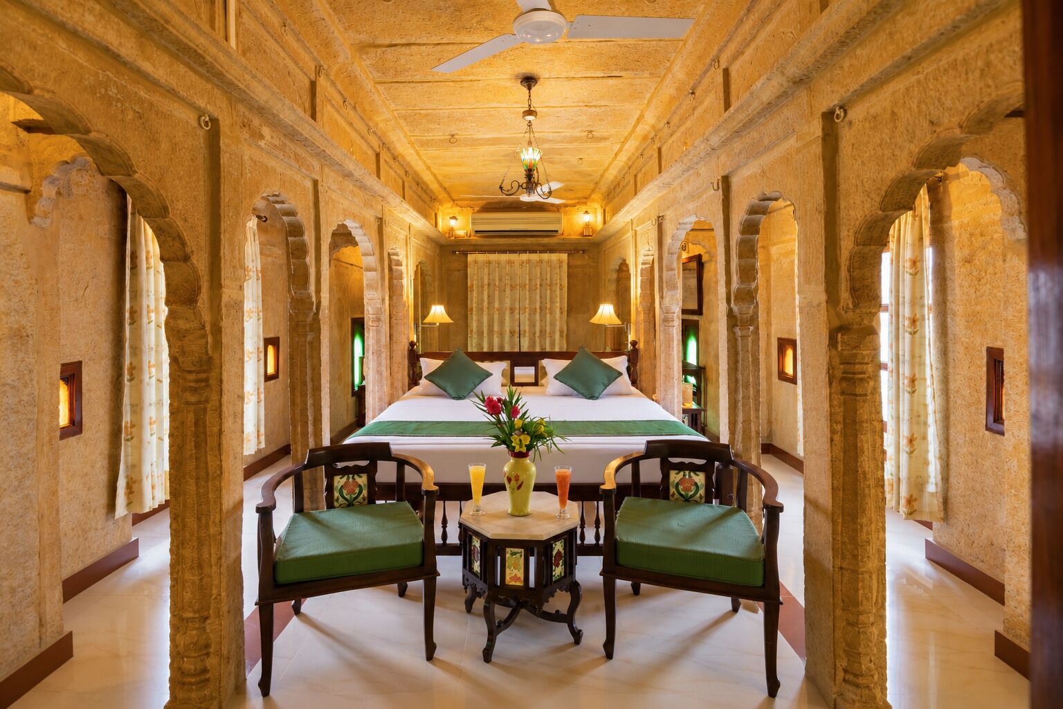 A hotel room with a large bed, two chairs, a small table, and a decorative vase.