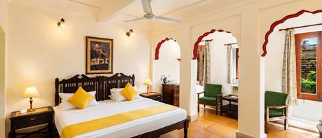 A hotel room with a large bed, a desk, a chair, a ceiling fan, and a view of the outdoors.