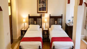A hotel room with two wooden beds, a painting on the wall, and a small table with a lamp.